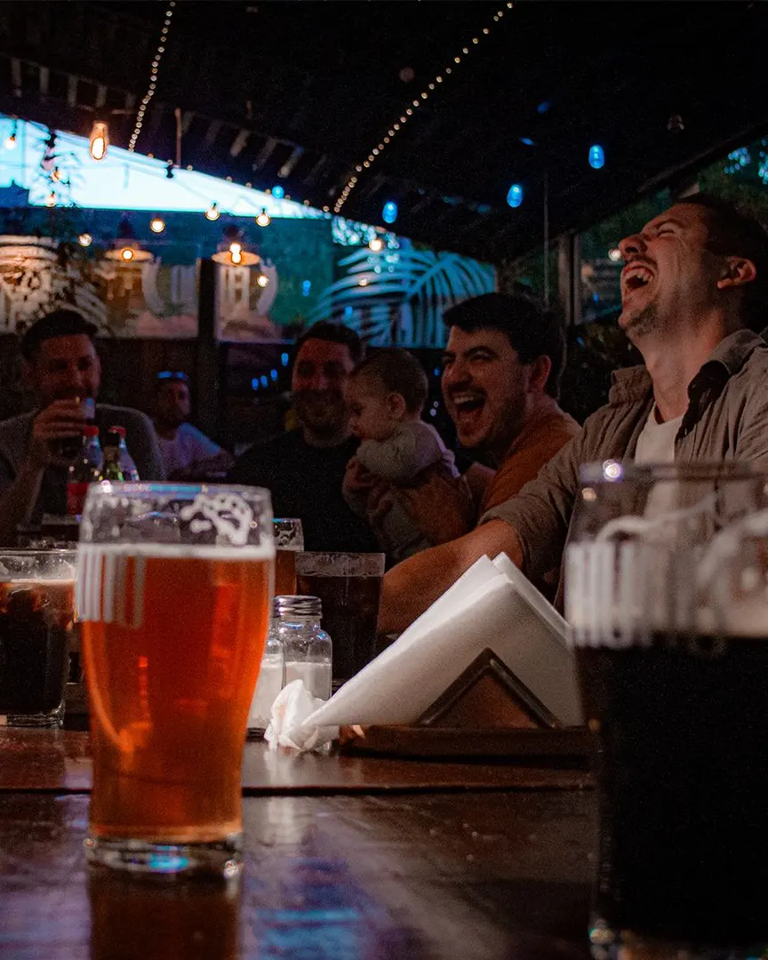 Una mesa larga de amigos riéndose con pintas