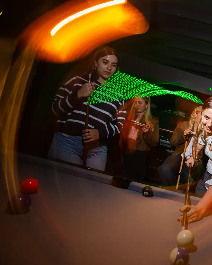Amigas jugando al pool entre luces verdes