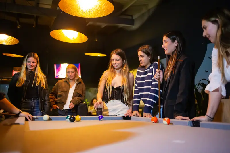 Amigas alrededor de la mesa de pool, bajo las lámparas