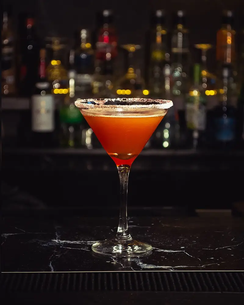 Un cóctel en copa con borde escarchado frente a la barra